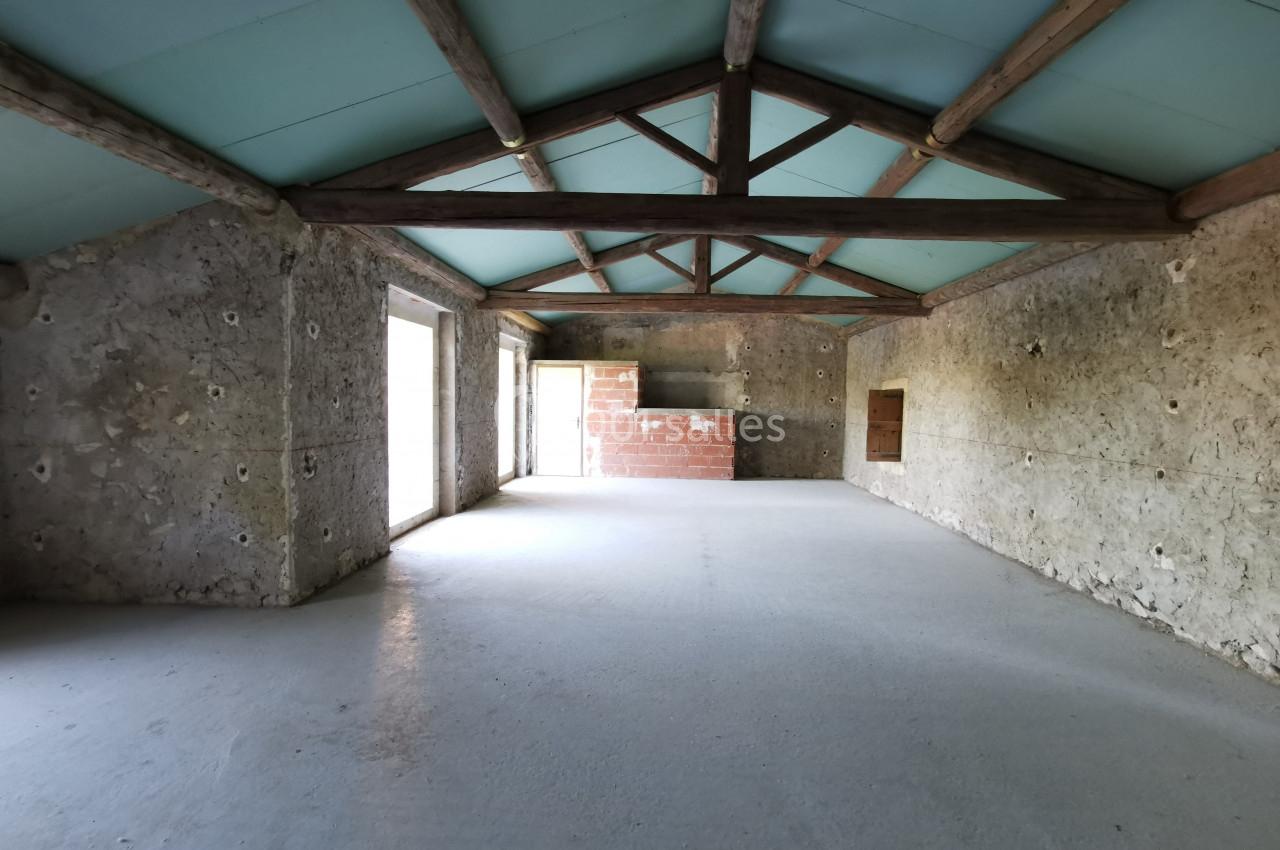 Intérieur d'une pièce vide avec murs en pierre, plafond en bois et toit bleu, éclairée par des ouvertures latérales.