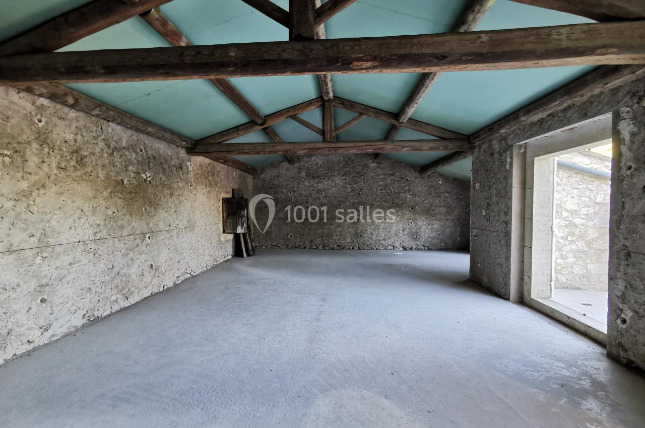 Intérieur d'une pièce vide avec murs en pierre, plafond en bois et ouvertures laissant entrer la lumière naturelle.