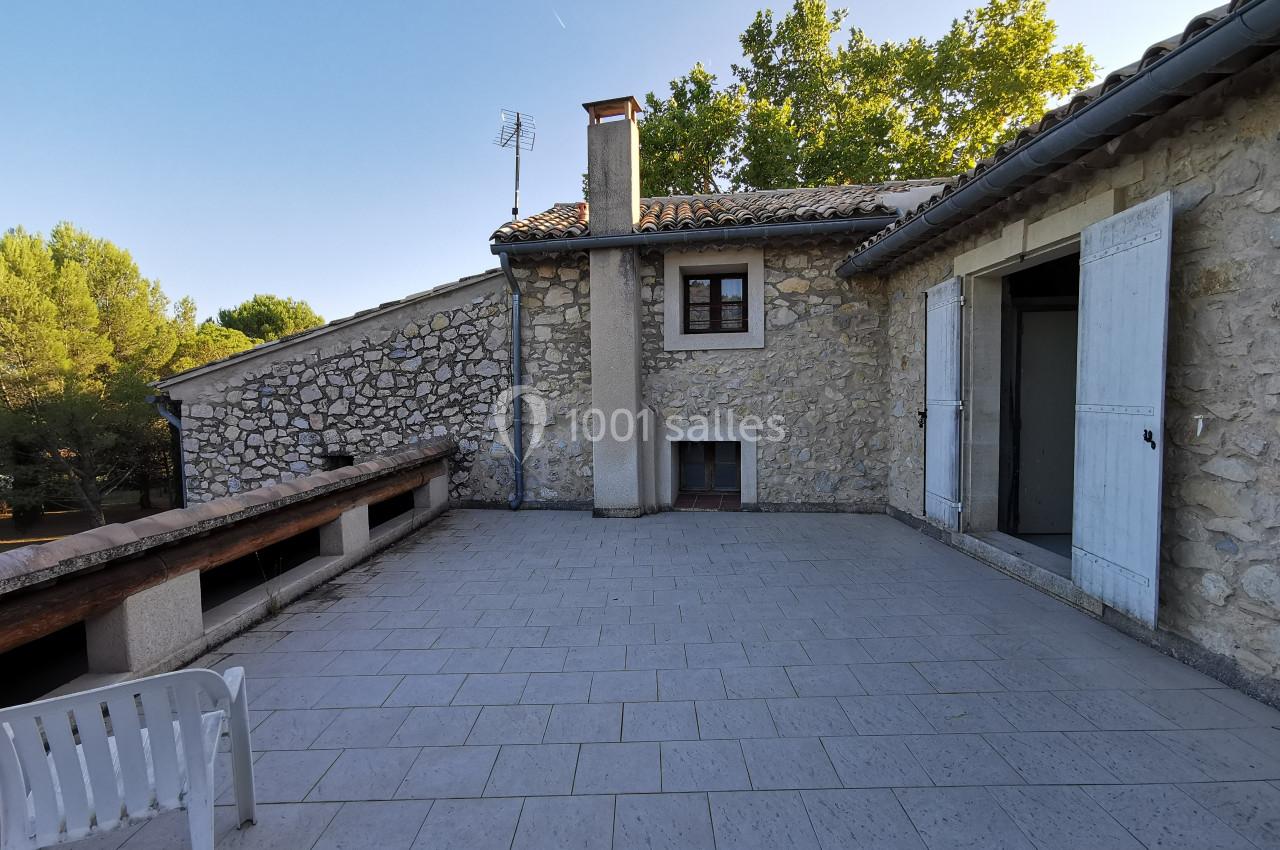 Terrasse en carrelage clair avec vue sur une maison en pierre, entourée de végétation et ciel dégagé.
