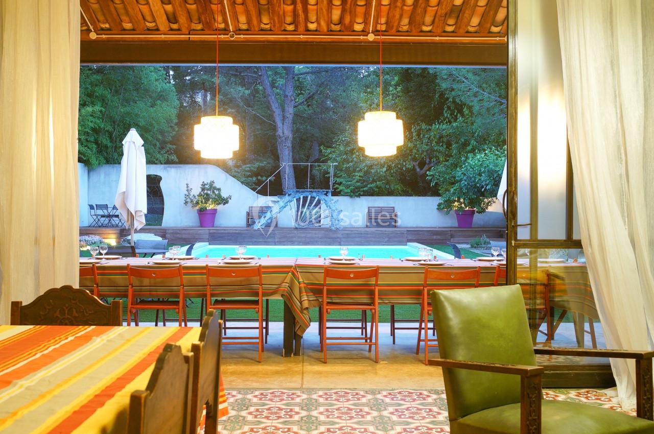 Salle à manger ouverte sur une terrasse avec piscine, tables dressées, chaises alignées et éclairage chaleureux.