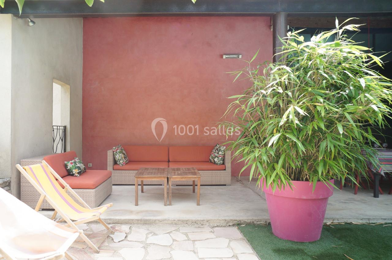 Salon de jardin avec canapés en osier, coussins colorés, table basse en bois et grand bambou dans un pot rose.