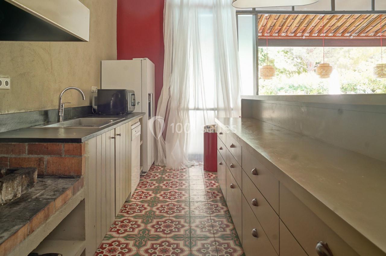 Cuisine lumineuse avec plan de travail en bois, évier en inox, micro-ondes et sol en carreaux colorés.