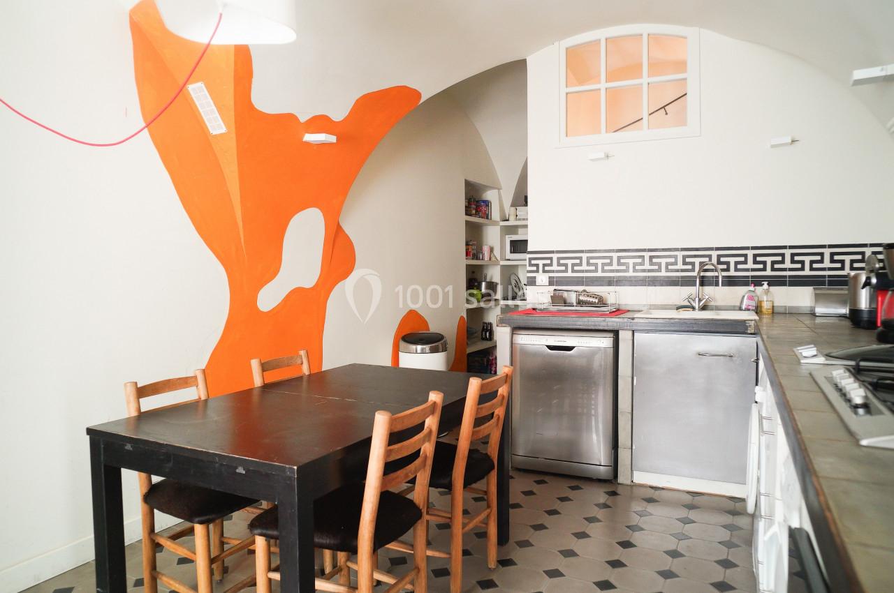 Cuisine avec table en bois, chaises, lave-vaisselle, plan de travail et mur décoratif orange vif.