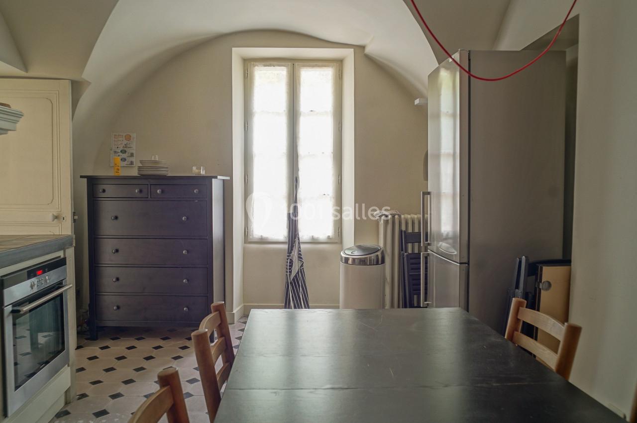 Cuisine lumineuse avec table en bois, chaises, armoire noire, réfrigérateur, four encastré et fenêtre centrale.