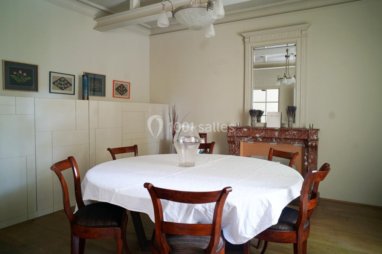Salle à manger avec table ronde couverte d'une nappe blanche, chaises en bois, cheminée en marbre et miroir mural.
