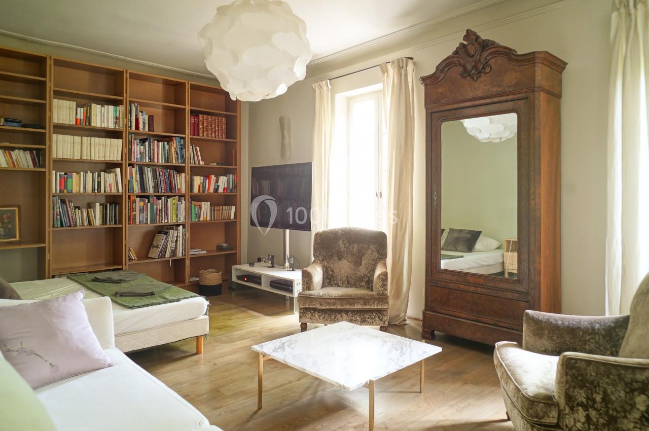 Salon lumineux avec bibliothèque en bois, canapé blanc, fauteuils, table basse en marbre et armoire ancienne avec miroir.