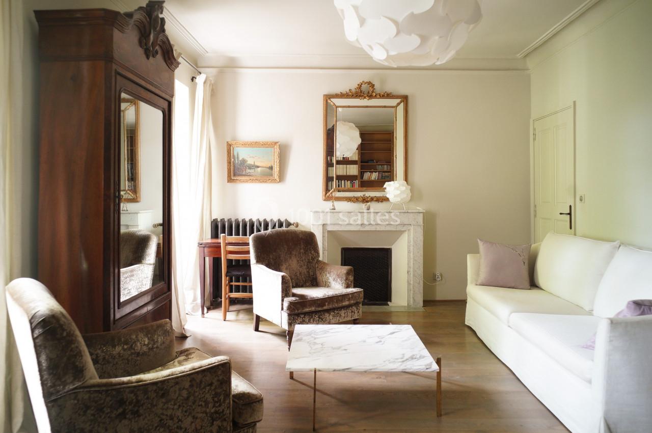 Salon lumineux avec mobilier classique, cheminée blanche, miroir doré, table basse en marbre et fauteuils rembourrés.