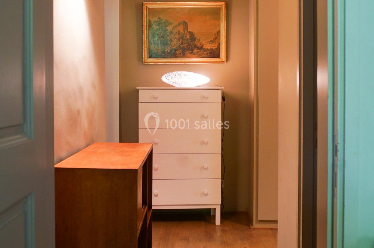 Couloir étroit avec parquet, commode blanche, lampe allumée, tableau encadré et meuble en bois.