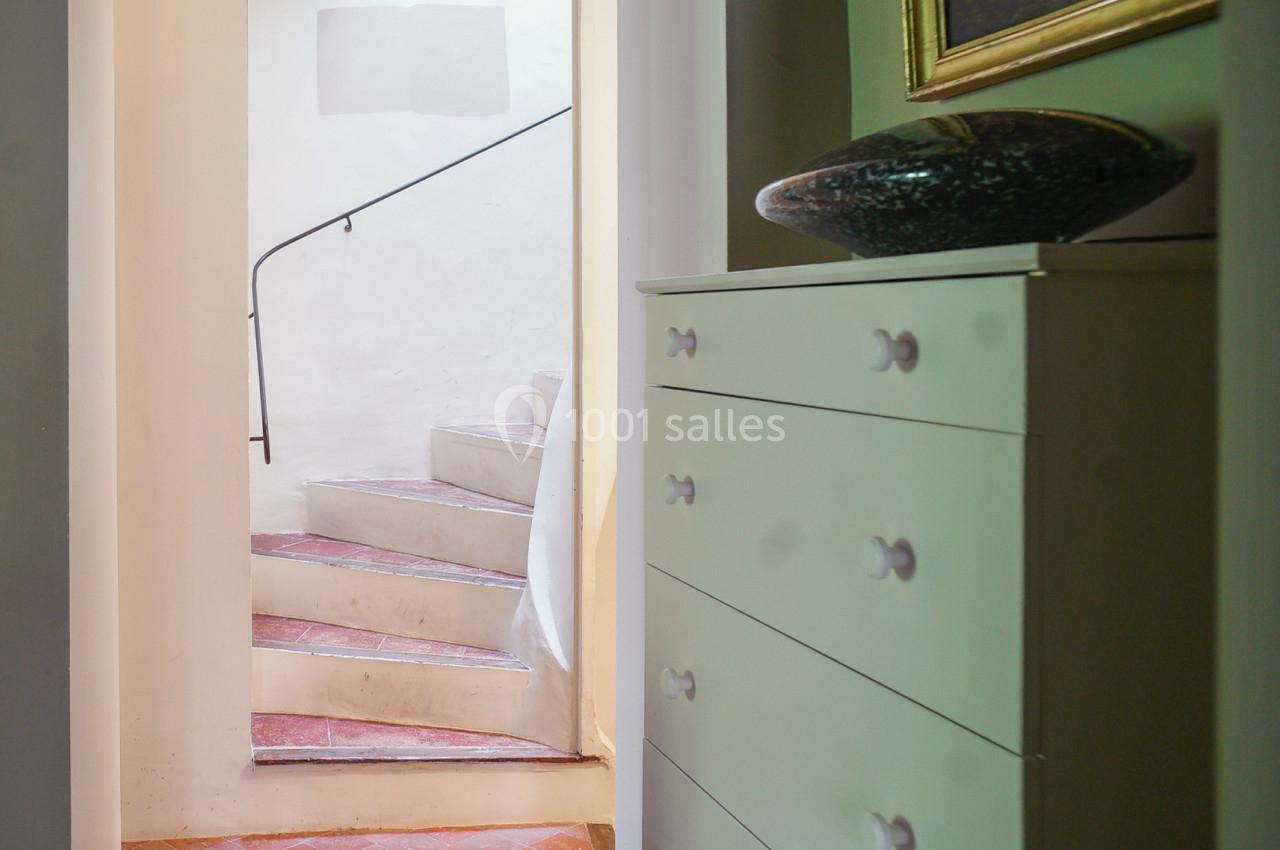 Escalier en colimaçon en pierre blanche éclairé par la lumière naturelle, avec une commode blanche au premier plan.