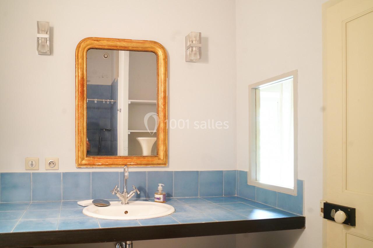 Lavabo avec plan de travail en carrelage bleu, miroir encadré en bois, et petite fenêtre apportant de la lumière.
