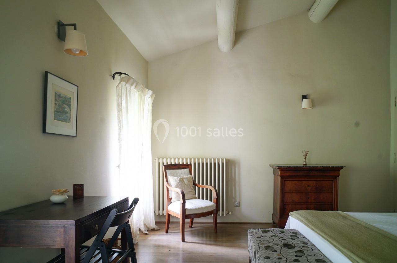 Chambre lumineuse avec murs clairs, lit, bureau en bois sombre, chaise, commode et fenêtre avec rideaux blancs.