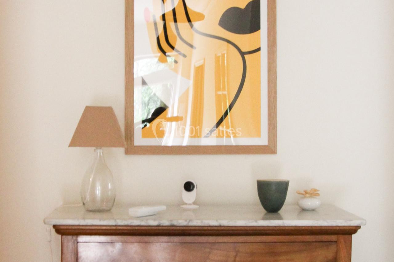 Commode en bois sur un sol carrelé, surmontée d'une lampe, d'objets décoratifs et d'un tableau abstrait encadré.