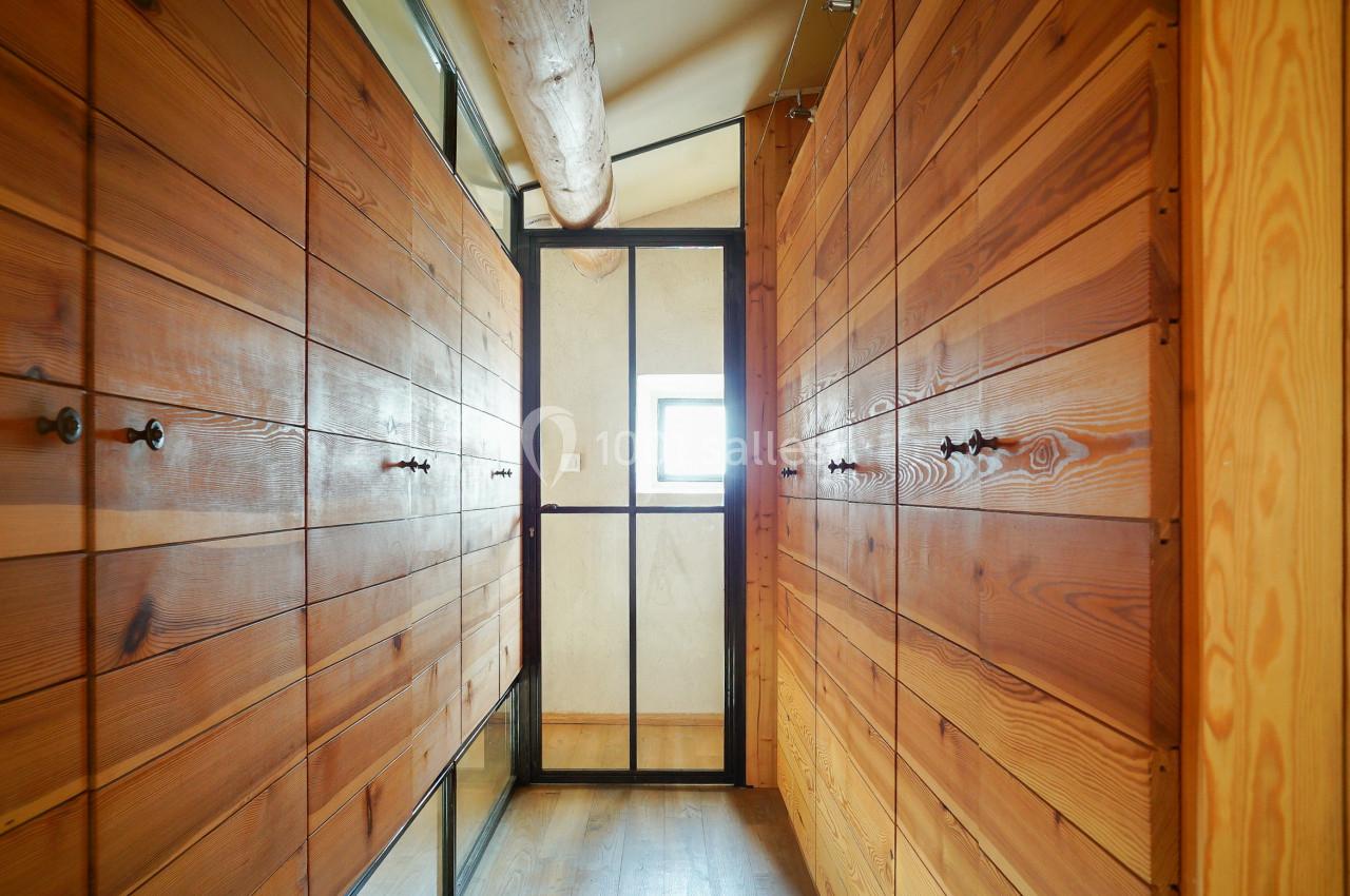Couloir étroit avec des murs en bois, une porte vitrée noire et une petite fenêtre laissant entrer la lumière.