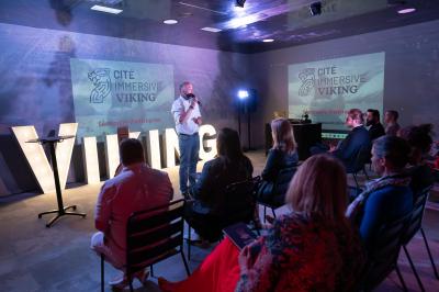 Une danseuse en tenue noire effectue une pose gracieuse sur une scène éclairée, devant un public attentif.