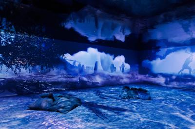 Une danseuse en tenue noire effectue une pose gracieuse sur une scène éclairée, devant un public attentif.