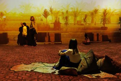 Une danseuse en tenue noire effectue une pose gracieuse sur une scène éclairée, devant un public attentif.