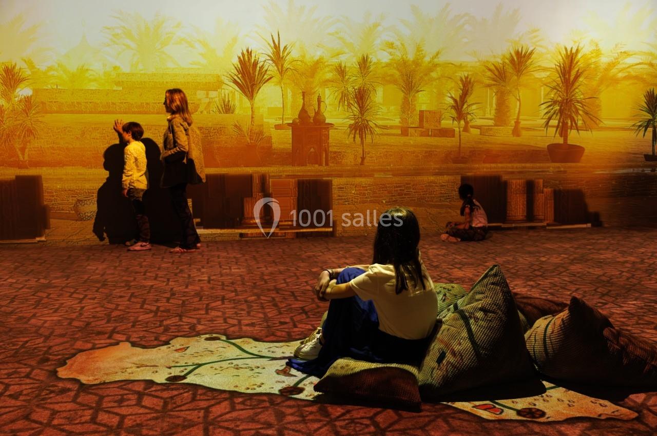 Une femme assise sur des coussins observe une projection immersive représentant un paysage désertique avec des palmiers.