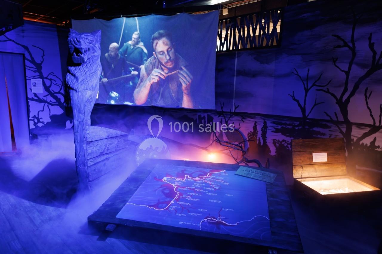 Scène immersive avec carte éclairée au sol, projection d'un homme, décor sombre et brumeux, ambiance mystérieuse.