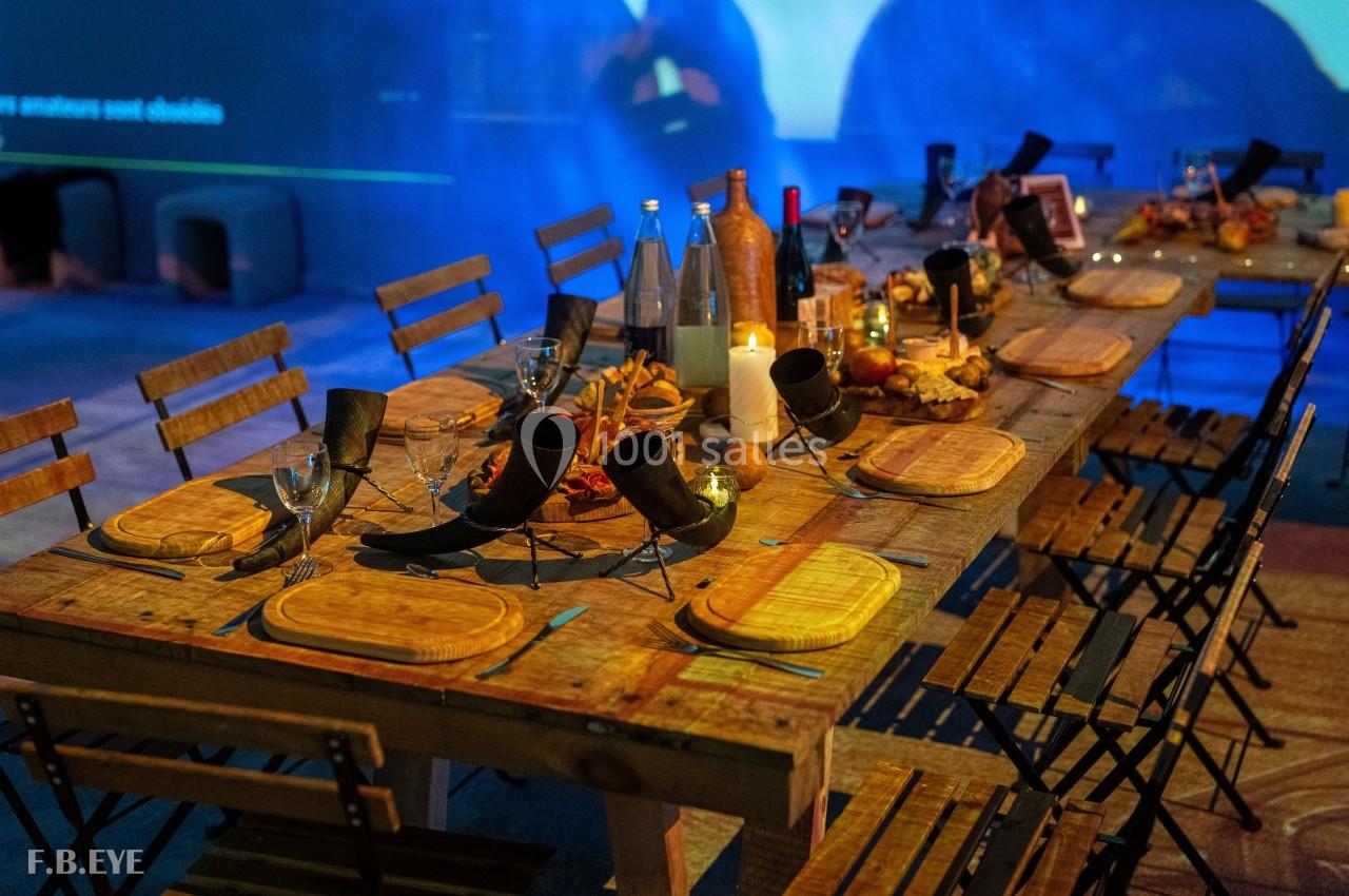 Table en bois rustique dressée pour un repas, avec cornes décoratives, assiettes en bois, bougies et bouteilles.