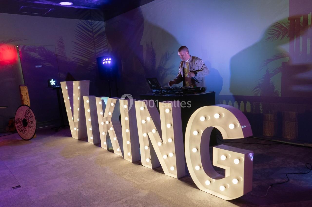 Un DJ mixe de la musique derrière des lettres lumineuses formant le mot ’VIKING’ dans une ambiance tamisée.