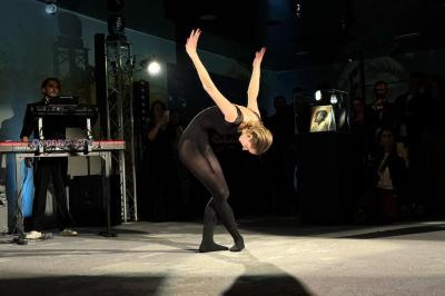 Une danseuse en tenue noire effectue une pose gracieuse sur une scène éclairée, devant un public attentif.