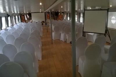 Salle de réception sur un bateau avec des tables dressées, des verres à champagne alignés et une vue sur l'eau en arrière…