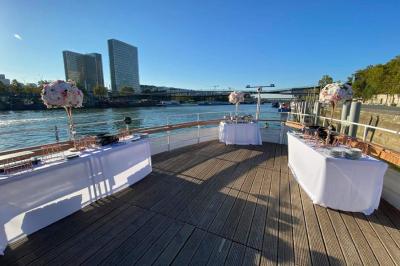 Salle de réception sur un bateau avec des tables dressées, des verres à champagne alignés et une vue sur l'eau en arrière…