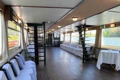 Salle de réception sur un bateau avec tables recouvertes de nappes blanches et plancher en bois clair.