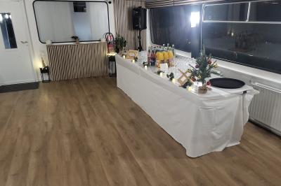 Salle de réception sur un bateau avec tables recouvertes de nappes blanches et plancher en bois clair.