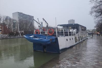 Salle de réception sur un bateau avec tables recouvertes de nappes blanches et plancher en bois clair.