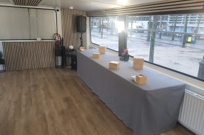 Salle de réception sur un bateau avec tables recouvertes de nappes blanches et plancher en bois clair.