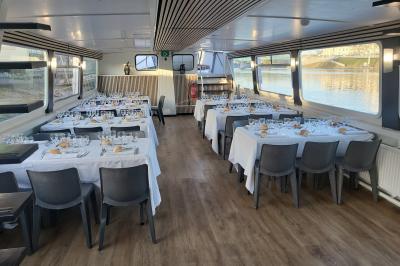 Salle de réception sur un bateau avec tables recouvertes de nappes blanches et plancher en bois clair.