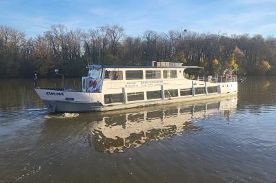 Salle de réception sur un bateau avec tables recouvertes de nappes blanches et plancher en bois clair.