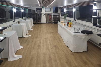 Salle de réception sur un bateau avec tables recouvertes de nappes blanches et plancher en bois clair.