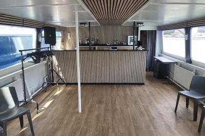 Salle de réception sur un bateau avec tables recouvertes de nappes blanches et plancher en bois clair.