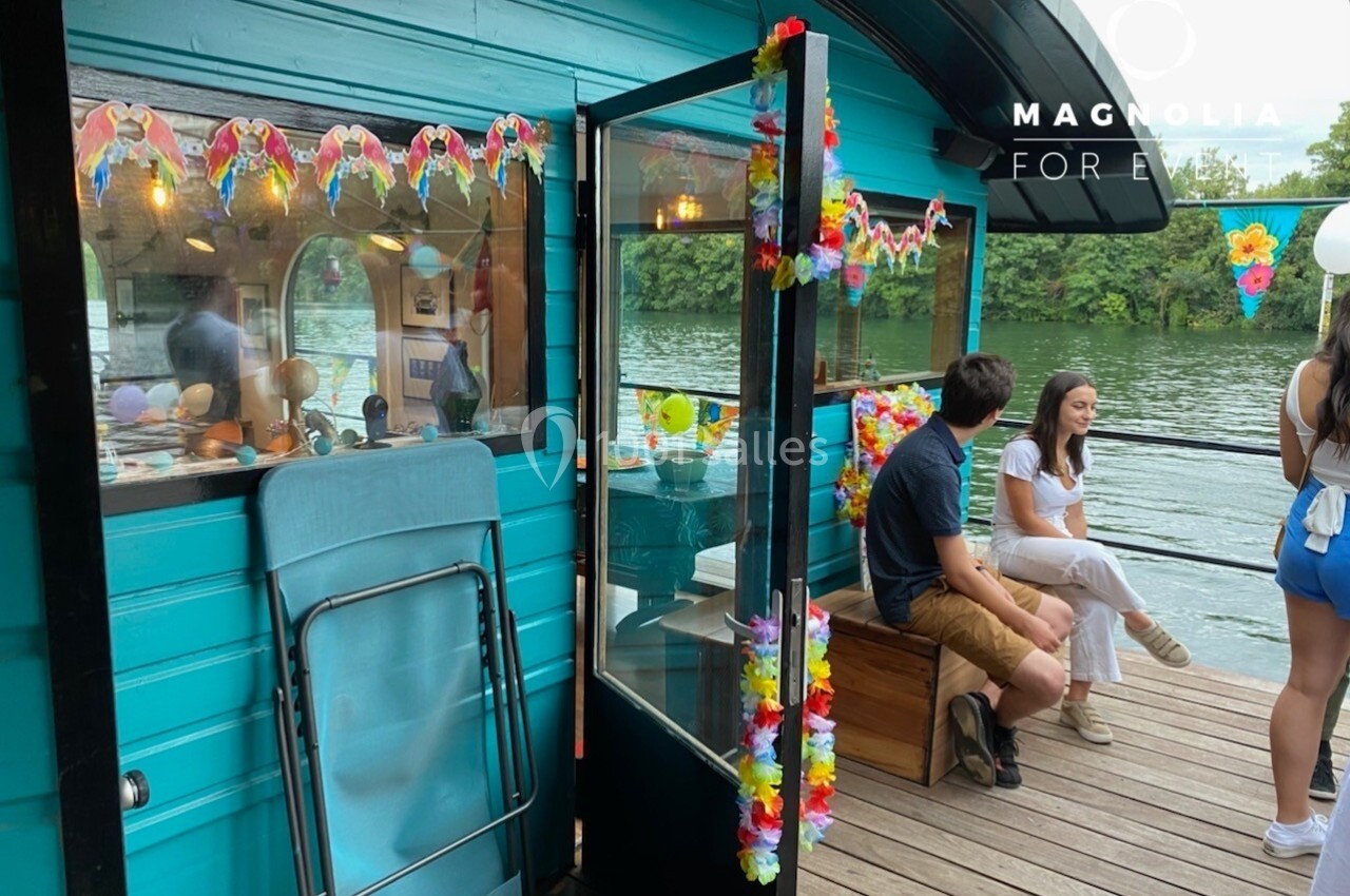 Personnes discutant sur une terrasse en bois décorée de guirlandes colorées, au bord d'une rivière.
