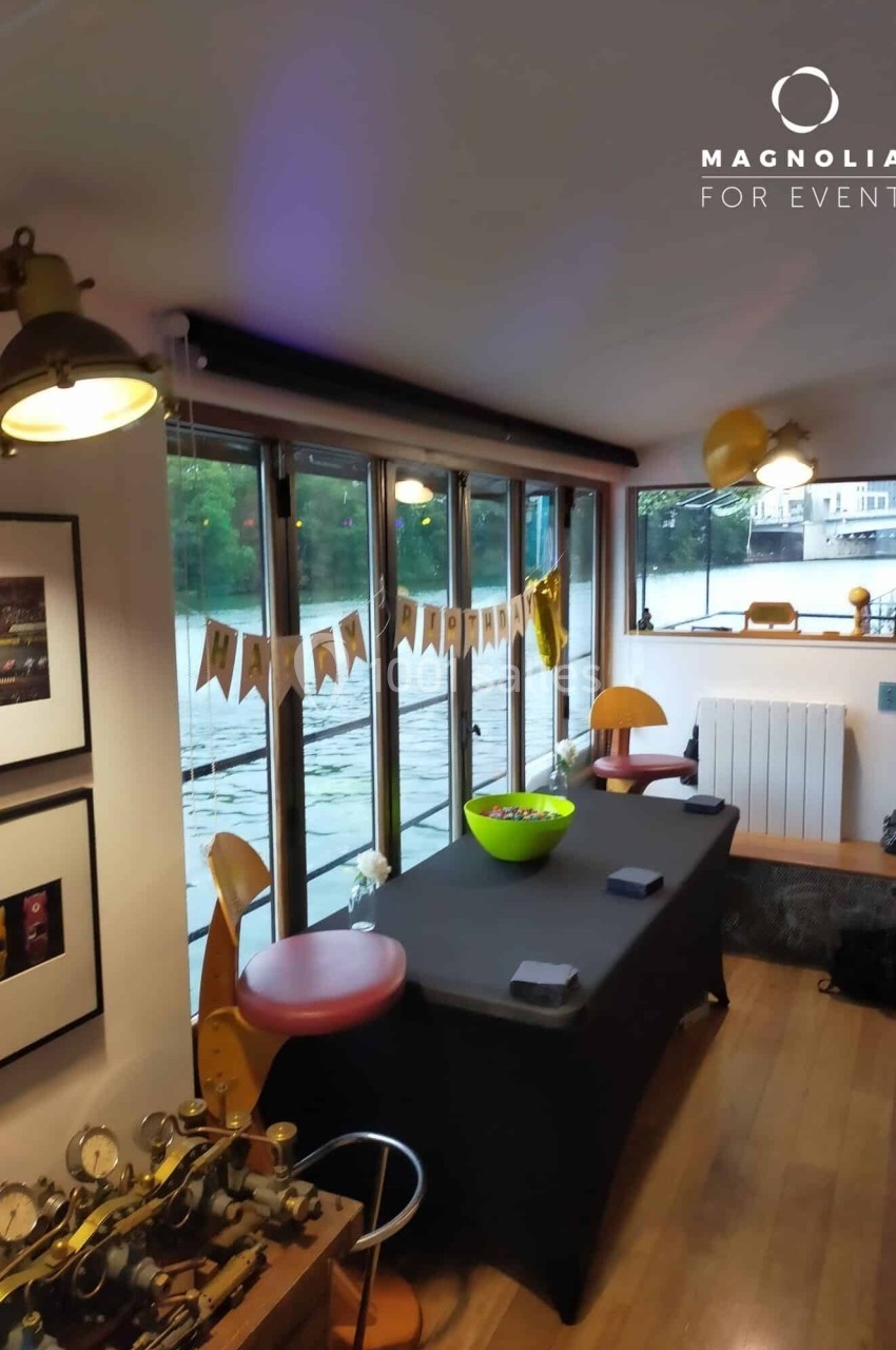 Salle décorée avec vue sur l'eau, table noire avec bols, guirlande suspendue et lumière naturelle.
