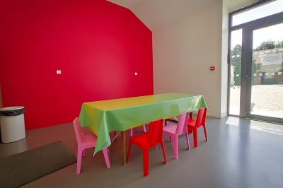 Table recouverte d'une nappe verte entourée de petites chaises colorées dans une pièce aux murs rouges et blancs.