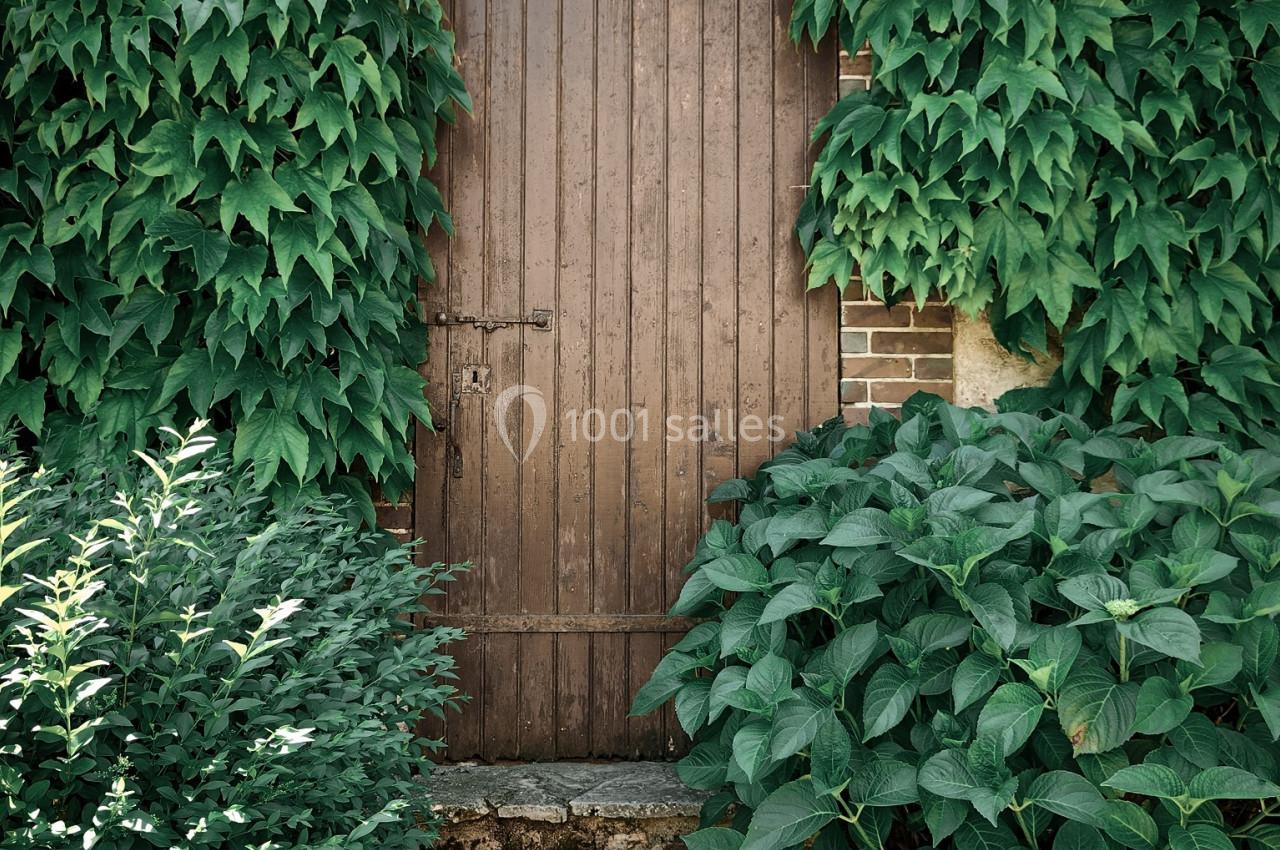 Porte en bois entourée de feuillage dense et de plantes grimpantes, avec des marches en pierre devant.