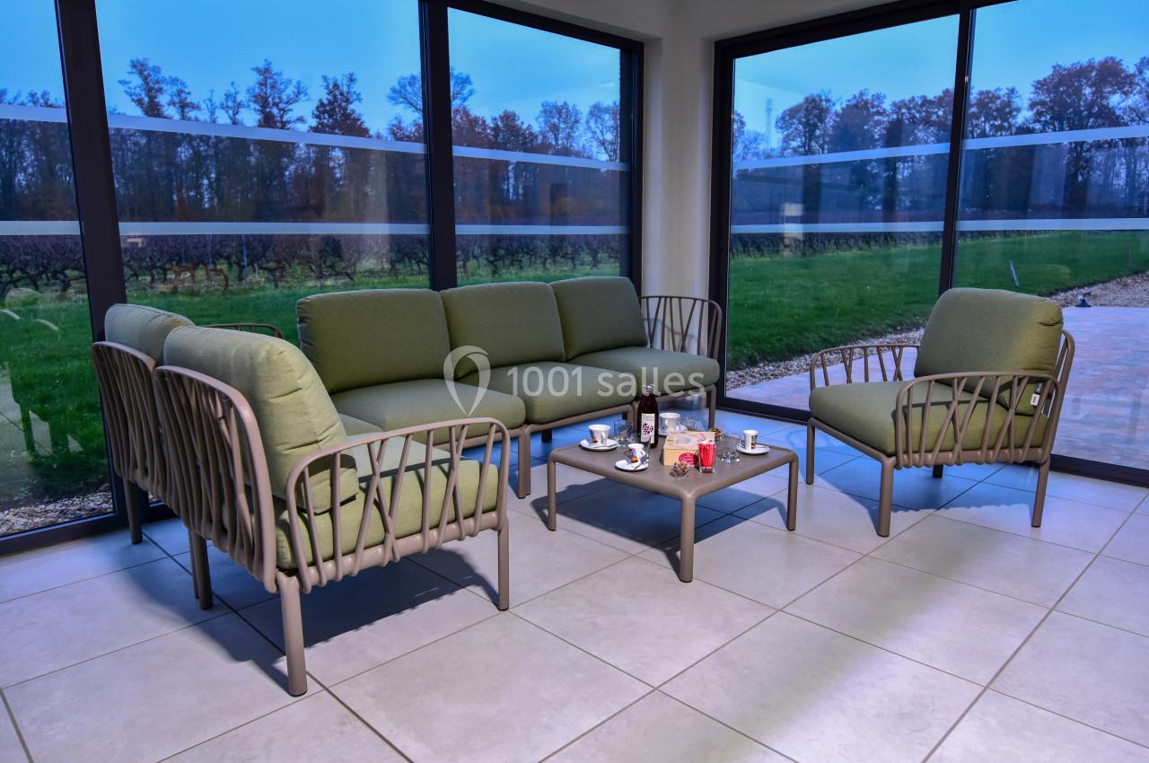 Salon de jardin avec fauteuils et canapé verts autour d'une table basse, situé dans une véranda avec vue sur un jardin.