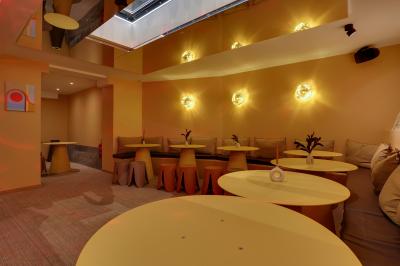 Une personne de dos prépare un cocktail avec un shaker dans un bar, portant un t-shirt blanc à motif orange.