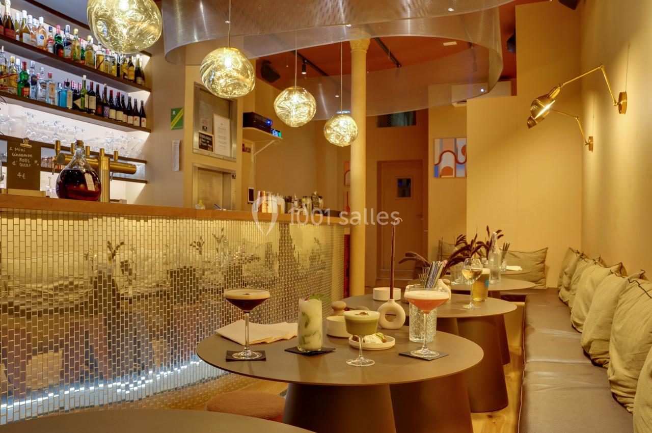 Intérieur d'un bar moderne avec tables basses, cocktails variés, éclairage chaleureux et décoration contemporaine.