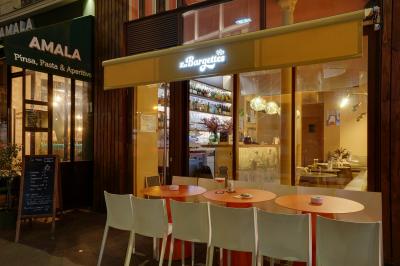 Une personne de dos prépare un cocktail avec un shaker dans un bar, portant un t-shirt blanc à motif orange.