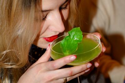 Une personne de dos prépare un cocktail avec un shaker dans un bar, portant un t-shirt blanc à motif orange.