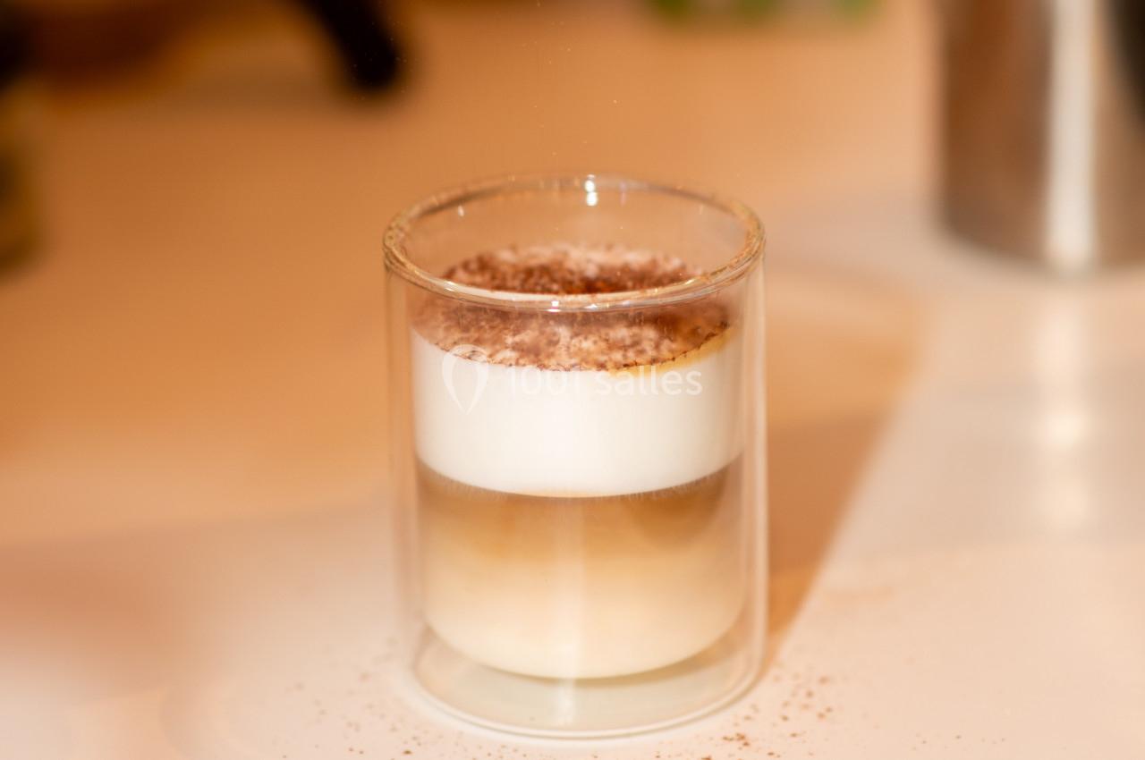 Verre transparent contenant une boisson en couches avec mousse blanche, café et lait, saupoudrée de cacao.