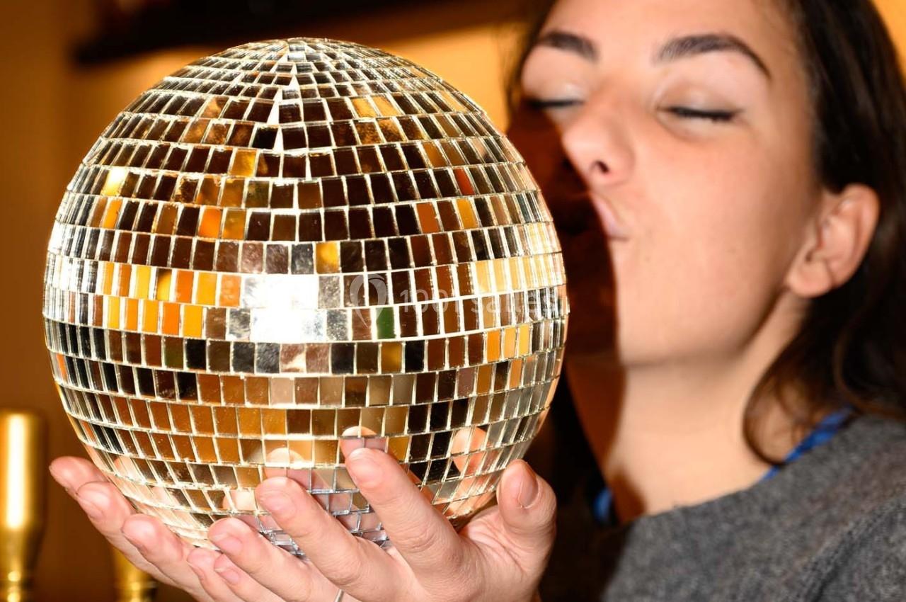 Une femme tenant une boule à facettes brillante dans ses mains, proche de son visage, en intérieur.