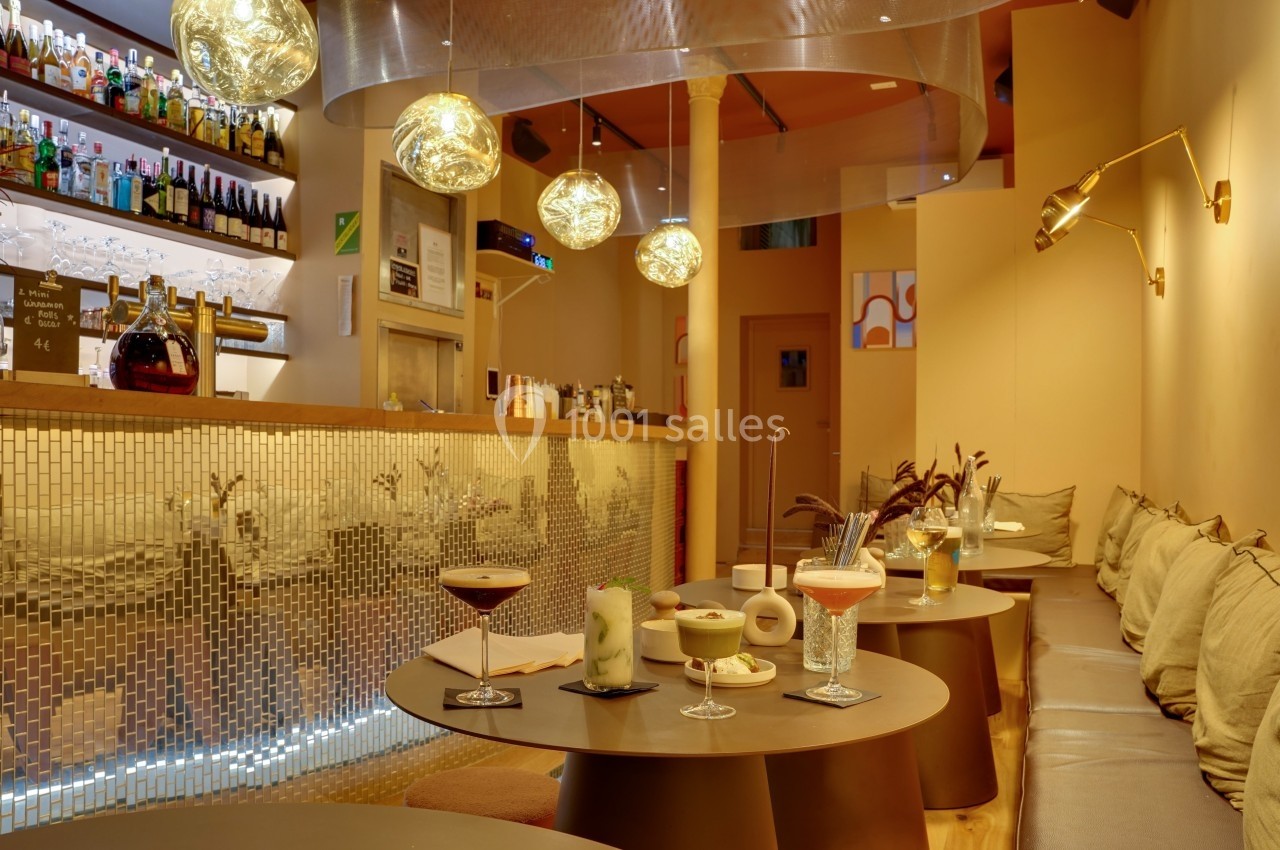 Intérieur d'un bar moderne avec tables rondes, cocktails variés, éclairage chaleureux et décor contemporain.