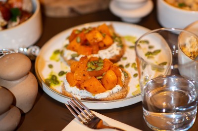 Tartines garnies de fromage frais, cubes de courge rôtie et graines, servies sur une table avec un verre d'eau.