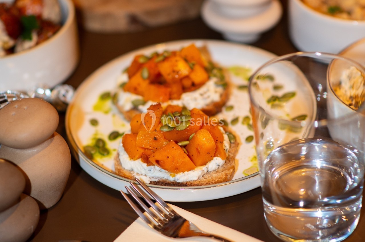Tartines garnies de fromage frais, cubes de courge rôtie et graines, servies sur une table avec un verre d'eau.