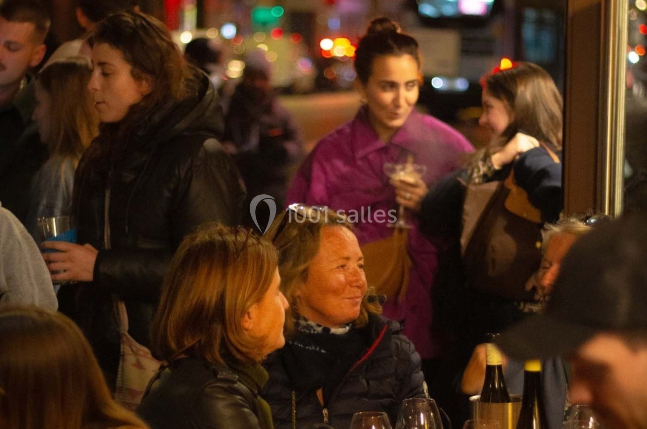 Groupe de personnes discutant et partageant des boissons dans un café animé en soirée.